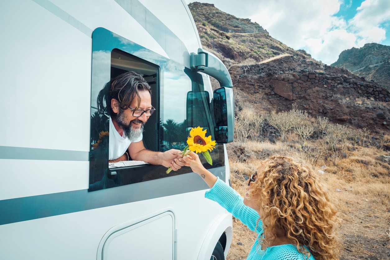 A man in an RV giving a flower to a woman outside. 